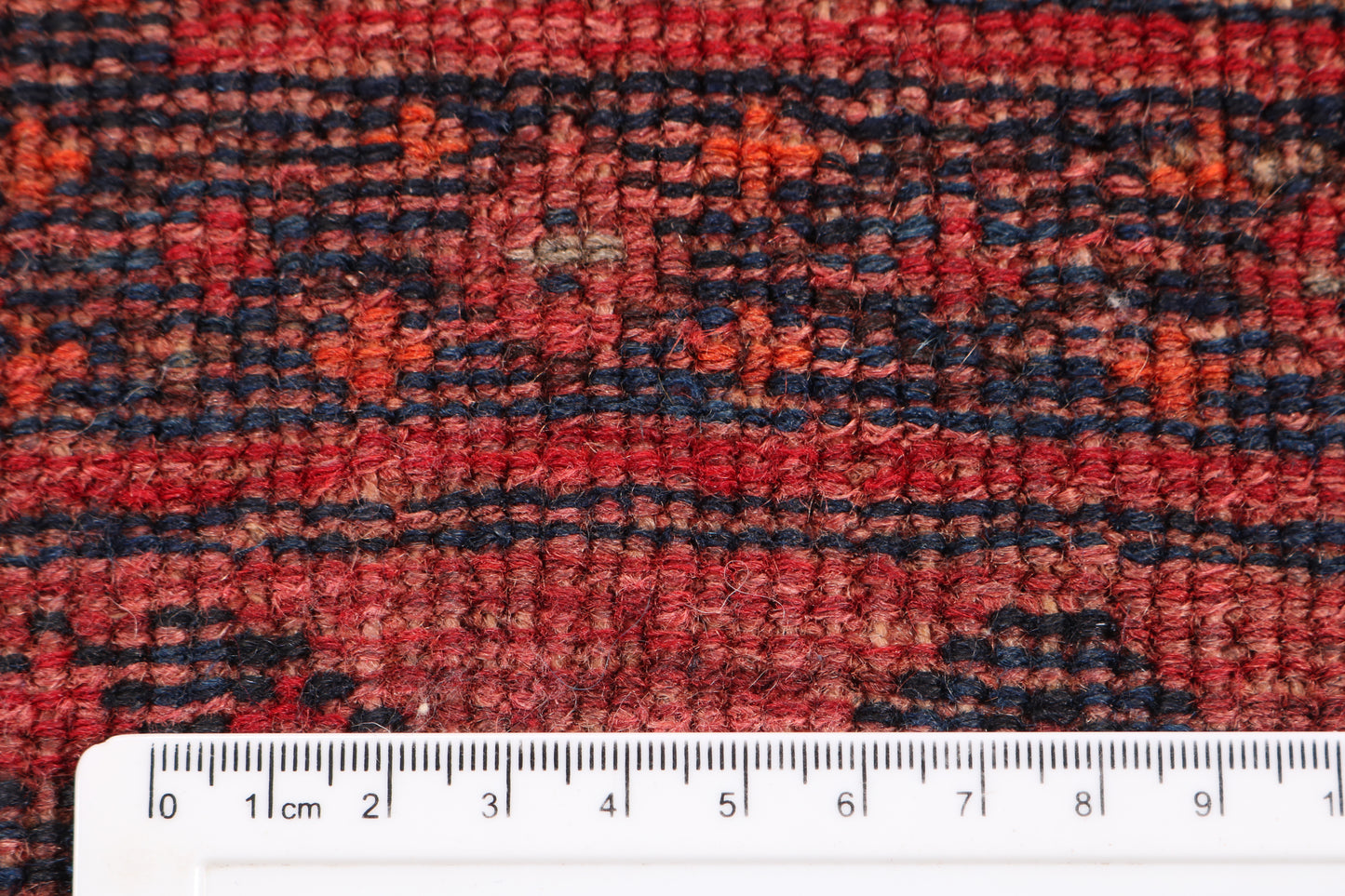 Close-up of a red and black patterned rug with a ruler for scale.