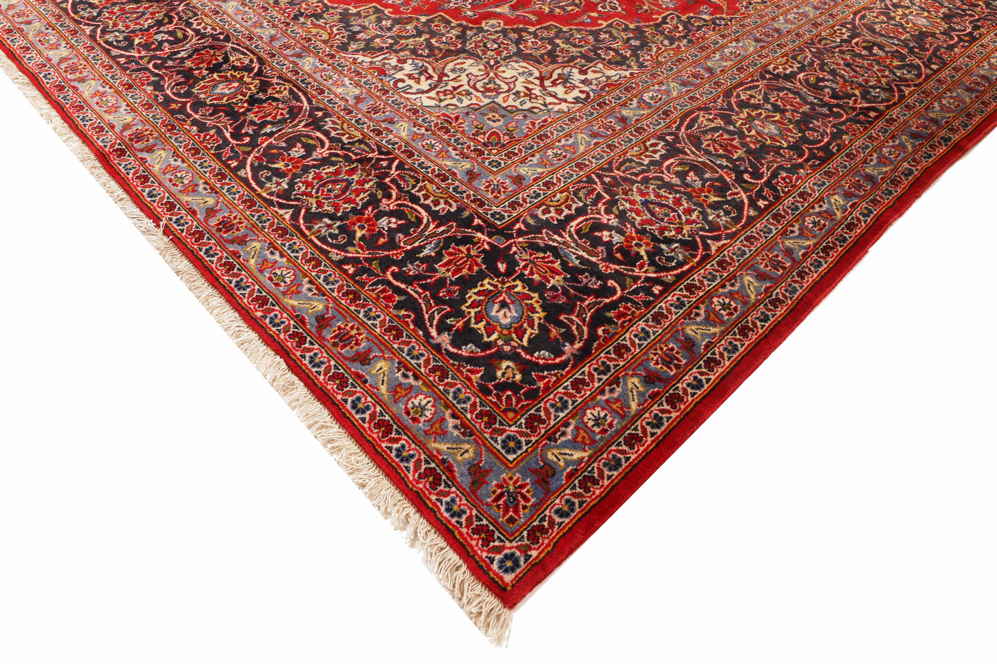Corner of a red and black patterned rug with tassels on a white background