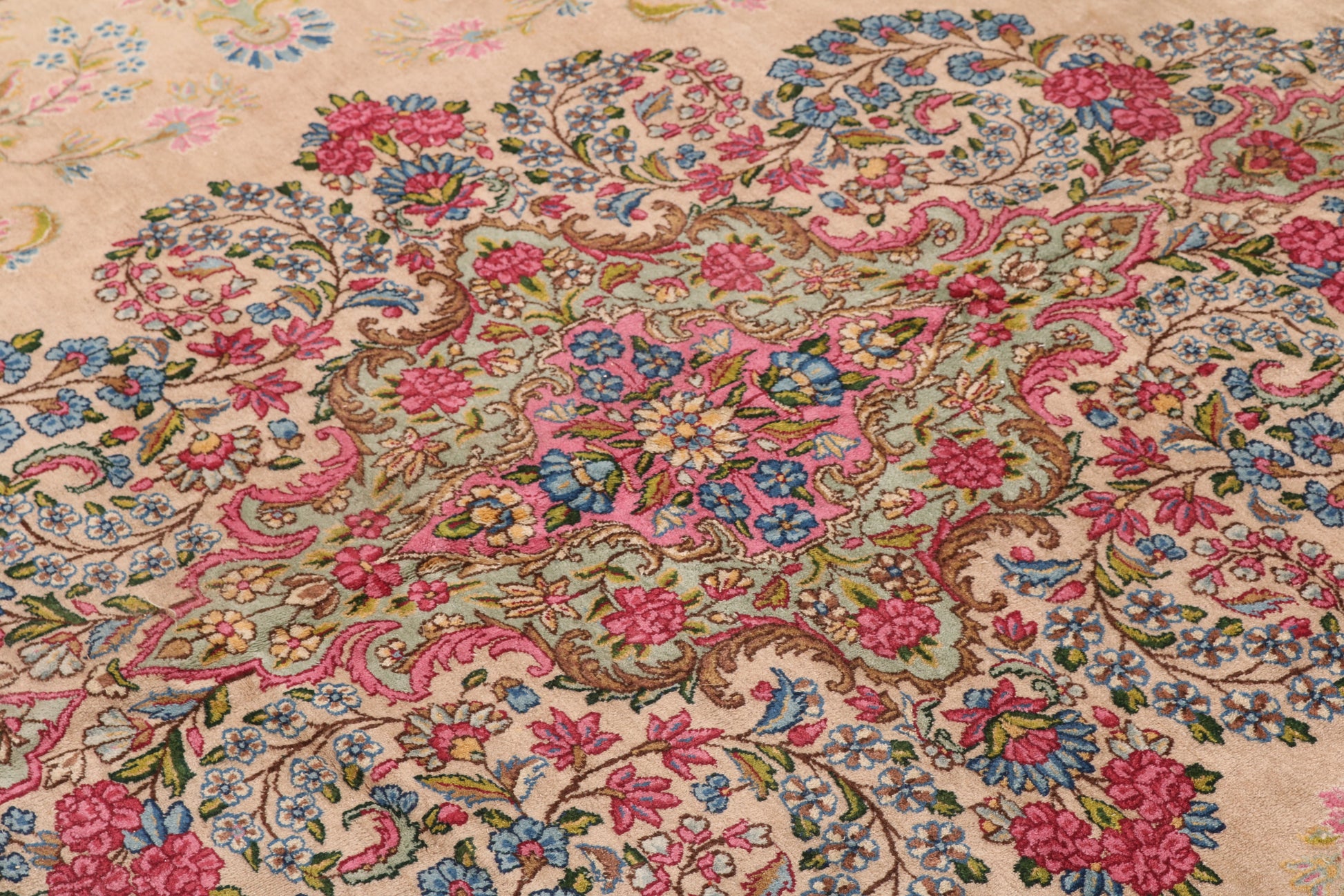 Close-up of a floral patterned rug with pink, blue, and green colors on a beige background.