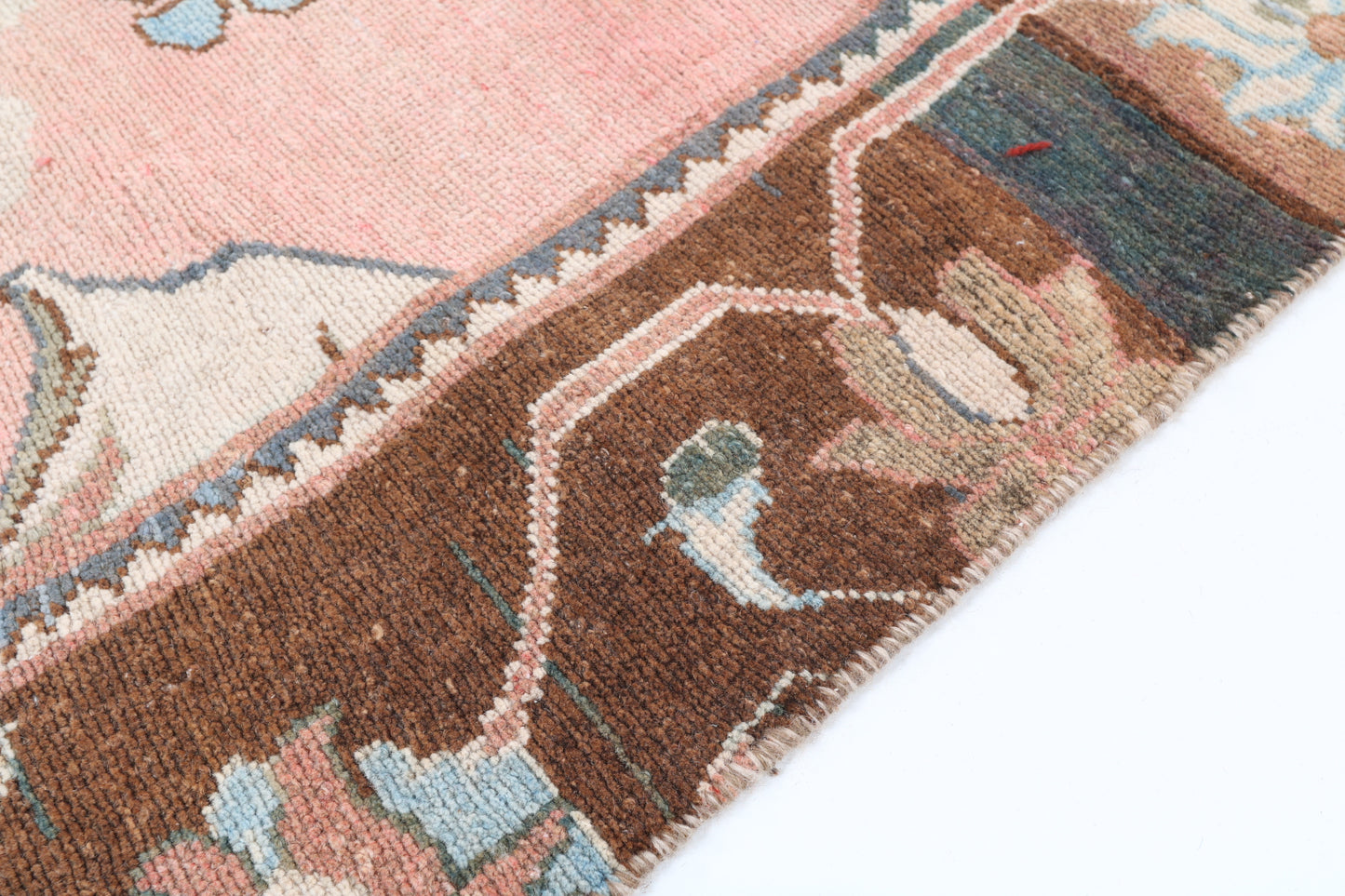 Close-up of a patterned rug with brown, pink, and blue colors on a white background