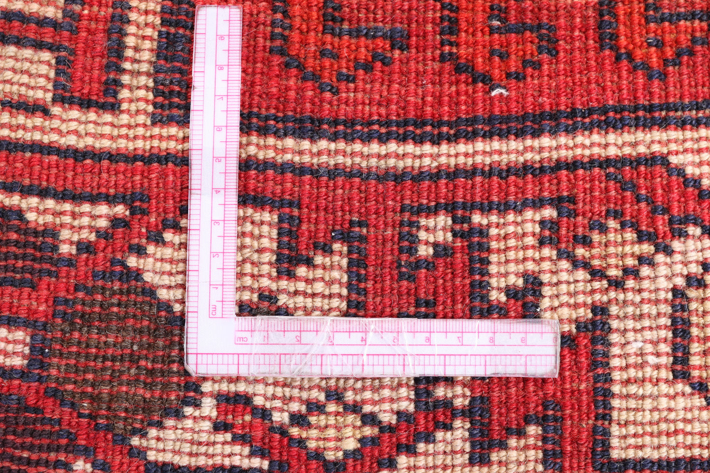 Close-up of a red and beige patterned rug with a measuring tape